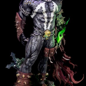 Pode incluir: Uma figura de ação detalhada do Spawn com um traje texturizado em preto e cinza, emblema branco no peito, capa vermelha escura, correntes prateadas, manoplas e grevas castanhas com espigões, fivela de cinto de caveira e base verde.