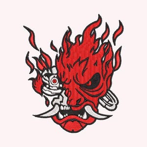 May include: Embroidered design featuring a red, flaming oni mask with black accents and white fangs. The design has a detailed, textured appearance, with flames and a stylized eye. The overall aesthetic is bold and striking, suitable for apparel or accessories.