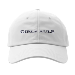 Puede incluir: Gorra de béisbol blanca con el texto "GIRLS RULE" bordado en azul marino.