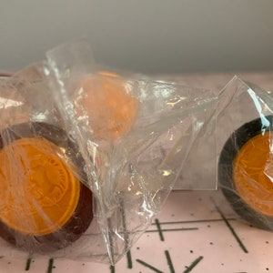 Puede incluir: Primer plano de cuatro piezas de juego redondas, de color naranja y marr&oacute;n, en una bolsa de pl&aacute;stico transparente. Las piezas tienen un dise&ntilde;o en relieve en la parte superior.