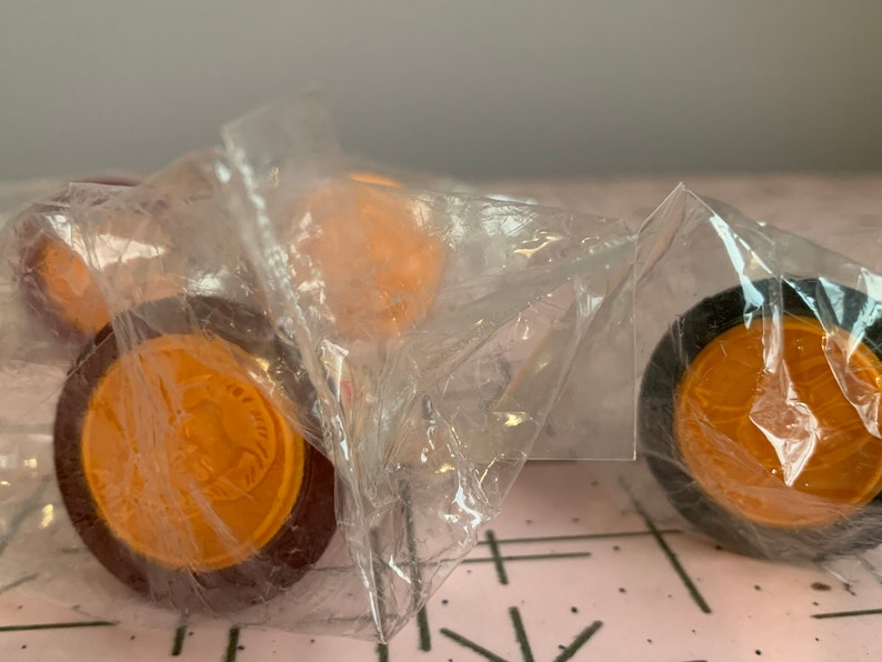 Puede incluir: Primer plano de cuatro piezas de juego redondas, de color naranja y marr&oacute;n, en una bolsa de pl&aacute;stico transparente. Las piezas tienen un dise&ntilde;o en relieve en la parte superior.
