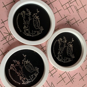 May include: Three black and white coasters with a map of Cape Cod, Massachusetts. The coasters have a white rim and the text "Cape Cod" and "Massachusetts" is printed on each coaster.