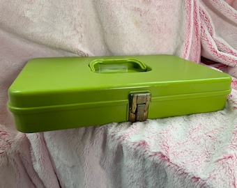 Puede incluir: Una caja de almacenamiento de metal verde brillante con un cierre dorado. La caja tiene un asa elevada en la parte superior.