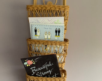 Op de afbeelding: Een drielaags wandorganizer van wilgentakken met een decoratieve bovenkant. De organizer is gevuld met kaarten, waarvan er één "Beautiful. Strong." zegt.