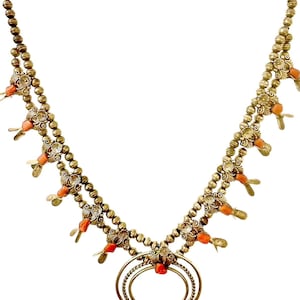 Puede incluir: Un collar de oro con un colgante de media luna y cuentas de coral. El collar está hecho de pequeñas cuentas redondas y tiene un diseño decorativo.