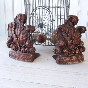 May include: A pair of wooden bookends with a carved leaf design. The bookends are brown and have a distressed finish.