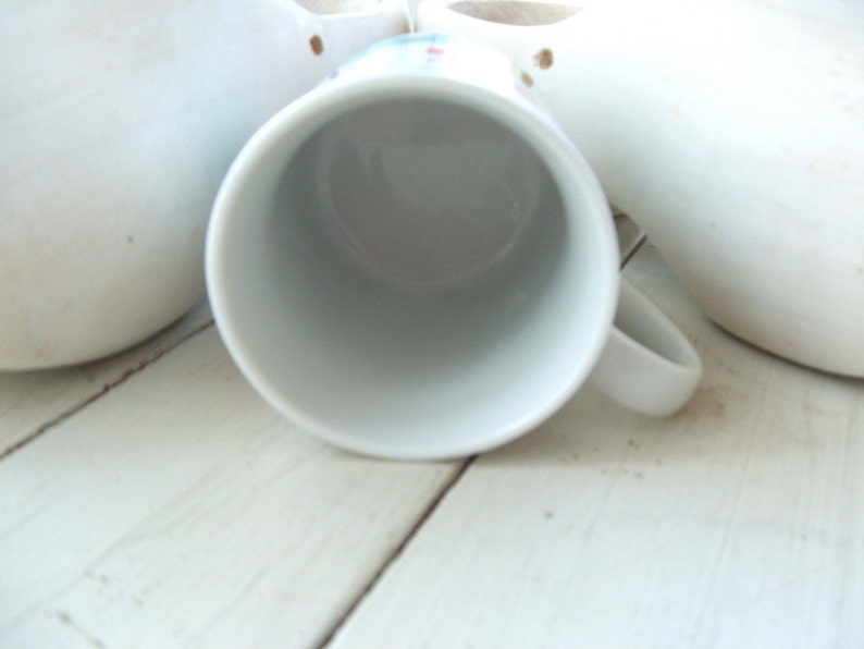 Puede incluir: Taza de caf&eacute; de cer&aacute;mica blanca con asa redondeada. La taza est&aacute; vac&iacute;a y se encuentra sobre una superficie blanca.