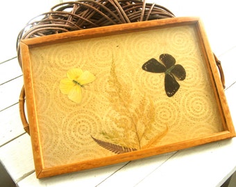 May include: A wooden tray with a light brown background featuring a pressed yellow butterfly and a black butterfly with green accents. The background has a circular pattern.