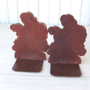 May include: A pair of wooden bookends shaped like trees with brown painted details. The bookends have a brown metal base.