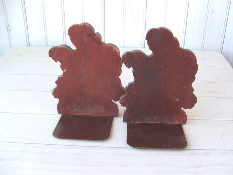 May include: A pair of wooden bookends shaped like trees with brown painted details. The bookends have a brown metal base.
