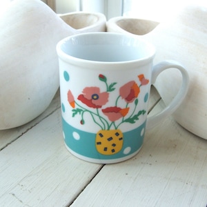 Puede incluir: Taza de cer&aacute;mica blanca con un patr&oacute;n de lunares azules y blancos y un dise&ntilde;o floral con flores rosas, rojas, amarillas y verdes. Las flores est&aacute;n en un jarr&oacute;n amarillo y negro.