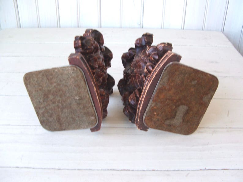 May include: A pair of wooden bookends with intricate carvings of leaves and flowers. The bookends have a dark brown finish and are in the shape of a half-circle. The bookends are sitting on a white surface.
