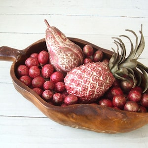 May include: A wooden bowl filled with red and gold decorative fruit, including a pear and a pineapple.