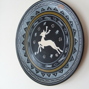 May include: A black ceramic plate with a white deer design and a gold and white geometric border.