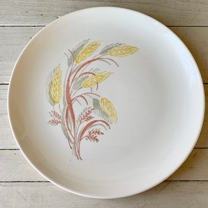 May include: A white ceramic dinner plate with a stylized design of wheat stalks in shades of yellow, green, and red.