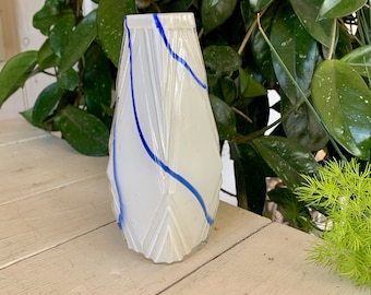 May include: A white glass vase with a textured surface and blue lines. The vase is shaped like a teardrop and has a narrow opening.