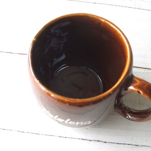 May include: A brown ceramic mug with a white inscription that reads "Solena".