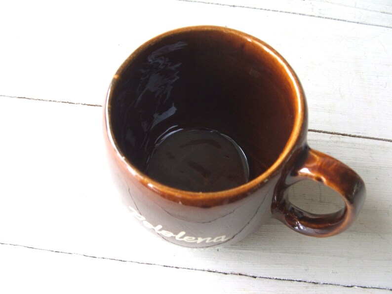 May include: A brown ceramic mug with a white inscription that reads "Solena".