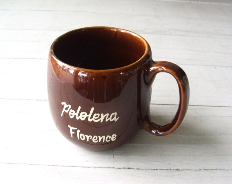 May include: A brown ceramic mug with a white inscription that reads "Pololena Florence".