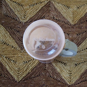 May include: A clear glass jar with a pink lid and a white label that says "Victoria Viane" with the number "4" printed on it. The jar is sitting on a woven brown and tan mat.