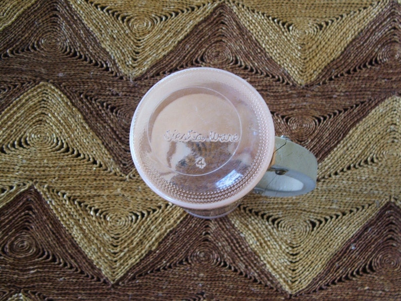 May include: A clear glass jar with a pink lid and a white label that says "Victoria Viane" with the number "4" printed on it. The jar is sitting on a woven brown and tan mat.
