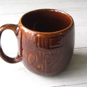 May include: Brown ceramic mug with a raised design and the word "HAWAII" on the side.