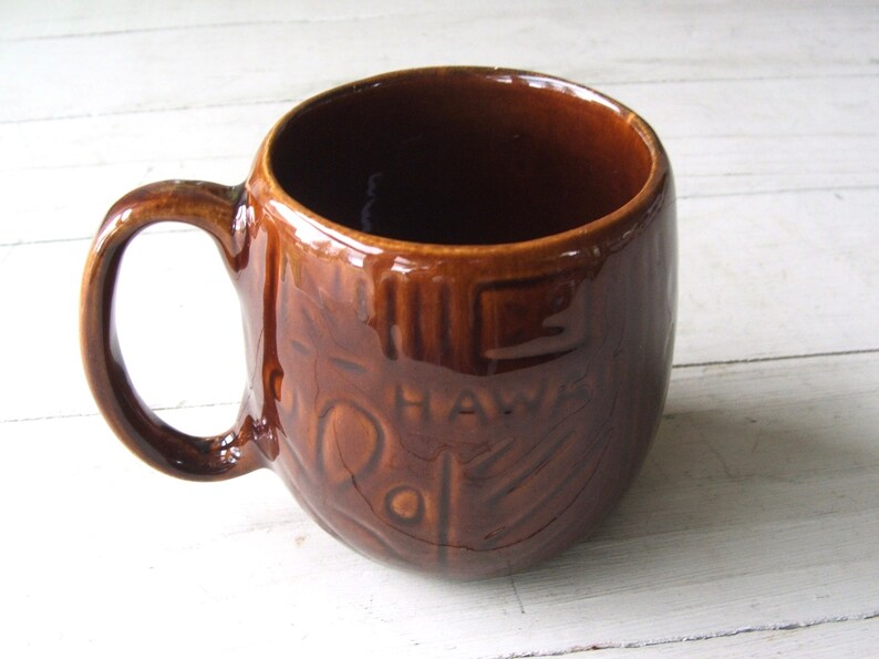 May include: Brown ceramic mug with a raised design and the word "HAWAII" on the side.