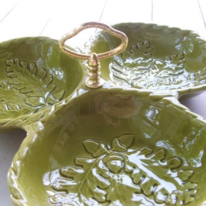 May include: A green ceramic serving dish with three sections, each featuring an embossed oak leaf design. The dish has a gold metal handle.