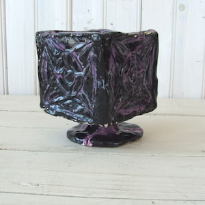 May include: A black and purple ceramic planter with a geometric design. The planter has a square base and a round top.