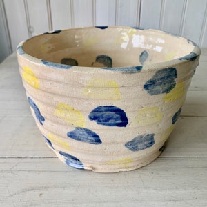 May include: A white ceramic bowl with a blue and yellow polka dot pattern. The bowl has a slightly rounded shape and is perfect for serving or storing items.
