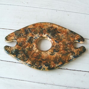 May include: A ceramic wine bottle holder with a brown, black, and blue speckled glaze. The holder has two cutouts for the bottle neck and a circular cutout for the bottle base.