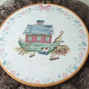 May include: A white fabric embroidery hoop with a colorful illustration of Noah's Ark with animals, flowers, and hearts around the border.