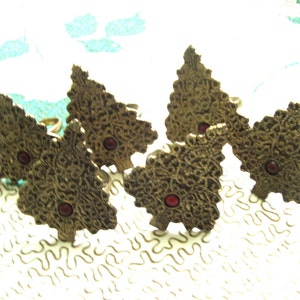 May include: Set of six gold-tone metal napkin rings shaped like Christmas trees with red jewel accents.