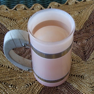 May include: A pink and white ceramic mug with a wooden handle. The mug has a silver band around the top and bottom. The mug is sitting on a woven placemat.