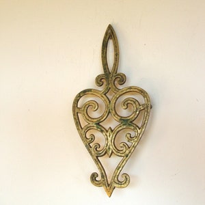 May include: A gold-colored metal trivet in the shape of a heart with intricate scrollwork.