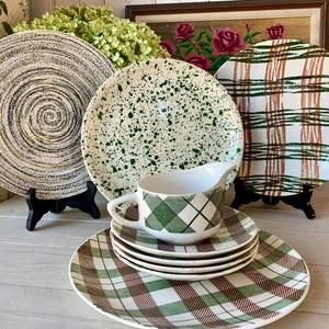 May include: Set of four vintage ceramic plates with different patterns. The plates feature a green and white speckled design, a brown and white plaid design, and a black and white swirl design. A white ceramic creamer with a green and white plaid design is also included.