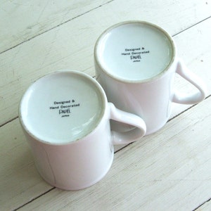 May include: Two white ceramic mugs with black lettering that reads "Designed & Hand Decorated Papel Japan".