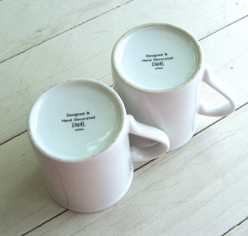 May include: Two white ceramic mugs with black lettering that reads "Designed & Hand Decorated Papel Japan".