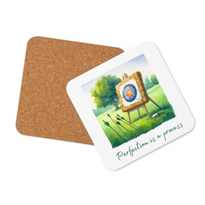 May include: A white coaster featuring a colourful target and arrows set against a green field. The text "Perfection is a process" is printed on the coaster.