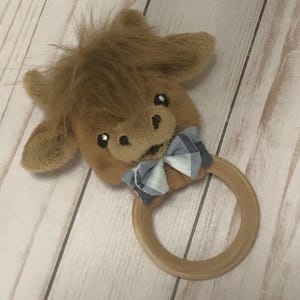 May include: A brown plush cow head with a blue and white checked bow tie attached to a wooden teething ring.