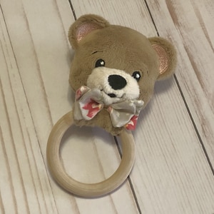 May include: A brown teddy bear head with a pink and white bow tie attached to a wooden teething ring.