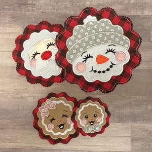 May include: Four Christmas-themed appliqued coasters. Santa Claus, a snowman, and two gingerbread people are featured. Each coaster has a scalloped edge with a red and black buffalo plaid pattern. The Santa has a white beard and red nose.