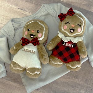 Puede incluir: Dos adornos de hombre de jengibre de peluche. Uno lleva una pajarita a cuadros rojos y negros y tiene el nombre "ADAM" bordado en la parte delantera. El otro lleva un vestido y un lazo a cuadros rojos y negros, con el nombre "ABBY" bordado en la parte delantera.