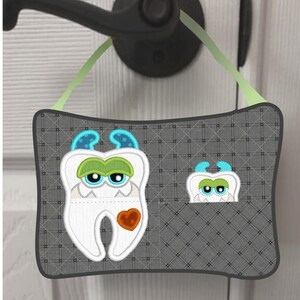 Peut inclure: Un porte-manteau gris et blanc avec un motif de monstre de dent. Le monstre de dent a des yeux verts, une bouche verte et un cœur rouge. Le porte-manteau a une poche sur le côté droit avec un motif de monstre de dent plus petit.