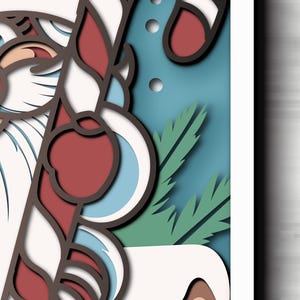 May include: A layered paper art piece featuring a stylized Santa Claus with a white beard and red hat, holding a red and white striped candy cane. The design includes green pine needles and circular accents against a blue background.