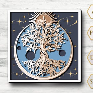 May include: A layered paper art piece featuring a tree design within a circle, set against a dark blue background with stars. The tree is detailed with light brown and white tones, with a sun at the top. The artwork is framed in a white square.