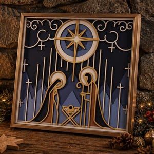 May include: A square framed wall art piece featuring a layered paper-cut nativity scene. The design includes a central gold star, stylized figures of two people standing over a manger, and a background of blue mountains, clouds, and crosses.