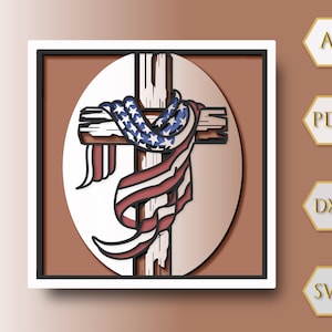 May include: A wooden cross with an American flag draped over it, set against a white oval background within a square frame. The flag features red and white stripes and blue stars. The artwork is a patriotic symbol.