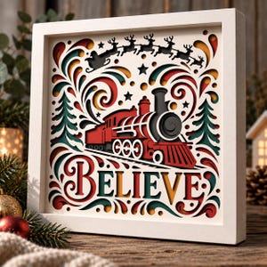 May include: A square white-framed layered paper art piece featuring a red steam locomotive, a silhouette of Santa and reindeer in flight, and the word BELIEVE in large decorative lettering, accented with green and yellow cutouts.