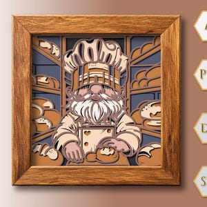 Puede incluir: Una pieza de arte en papel en capas enmarcada que presenta un gnomo panadero en una panadería. El gnomo lleva un gorro y delantal de chef, rodeado de pan. El marco es de un tono de madera cálido, y el fondo es una mezcla de azul y marrón.
